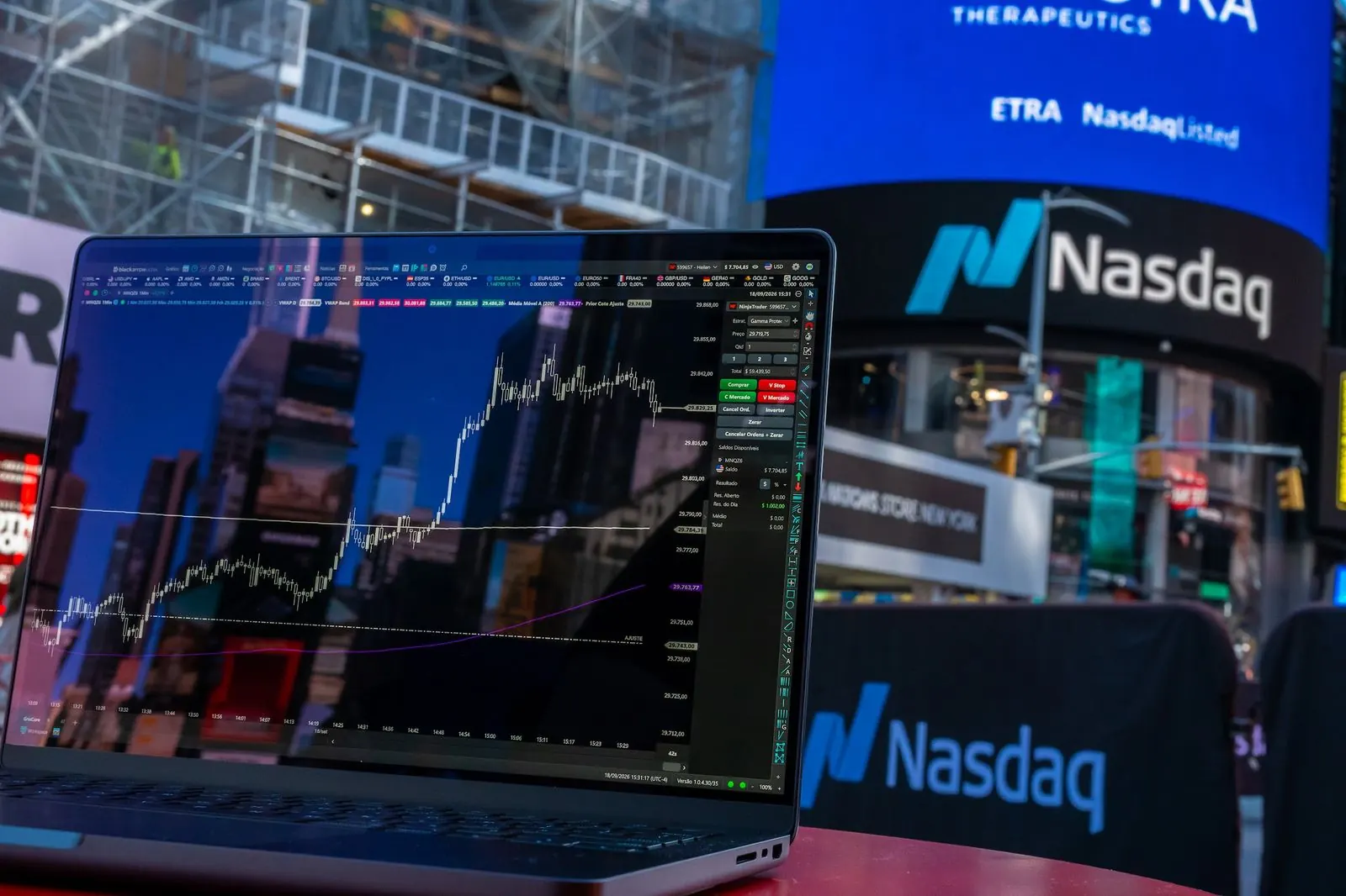 Notebook com gráfico de Nasdaq em frente ao painel da Nasdaq, na Times Square